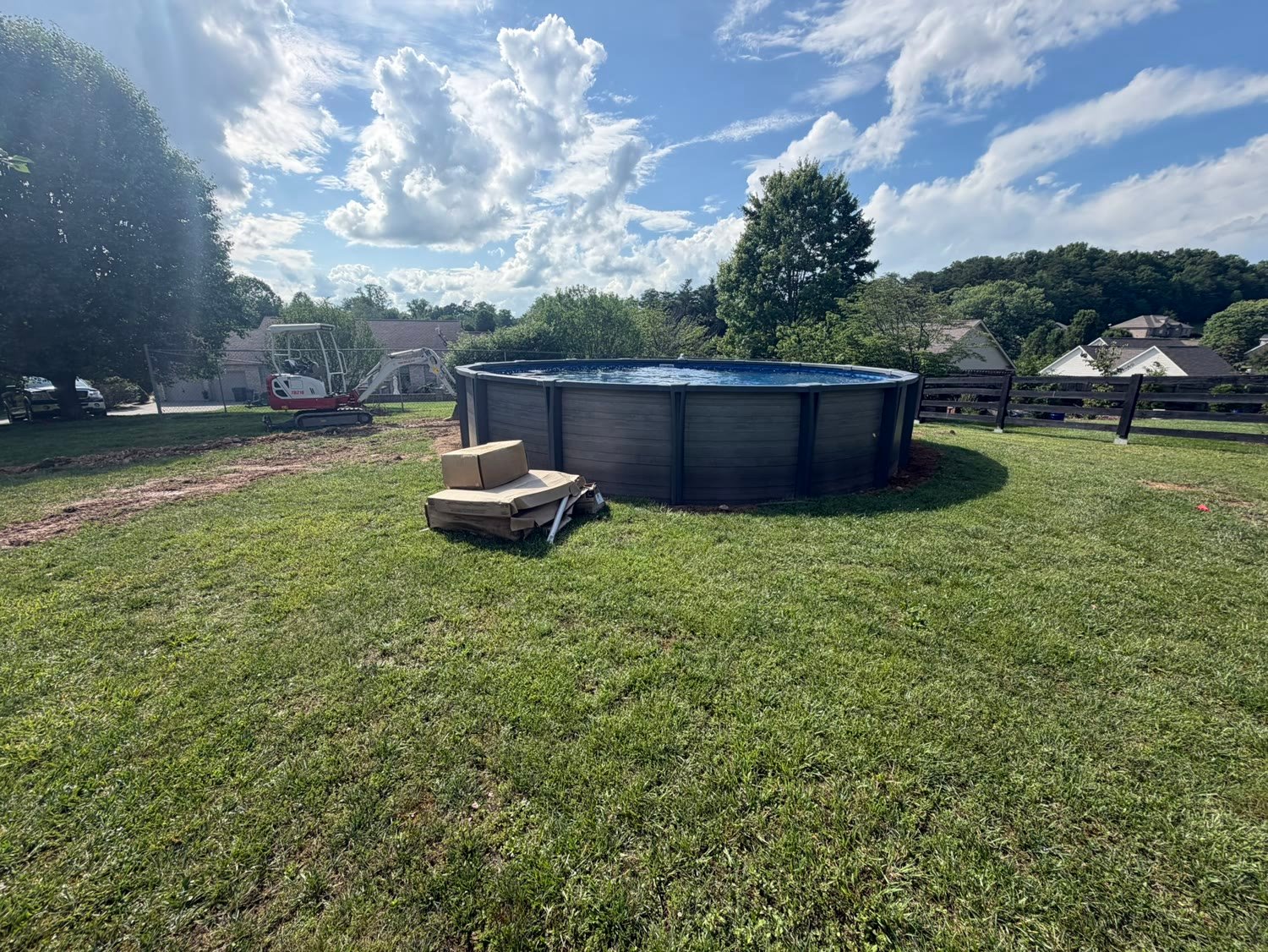 A bare back yard with a newly set above ground pool and a mini excavator parked behind it.