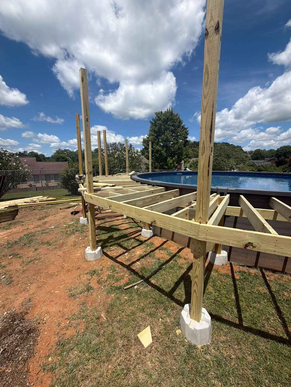 Deck framing under construction: pressure treated posts on concrete piers with joists running out to the pool.